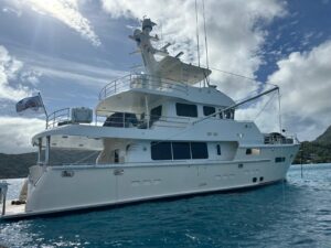 A cream colored Nordhavn 76 in Bora Bora being prepared by yacht delivery solutions a white could is visible and the water is clean and blue