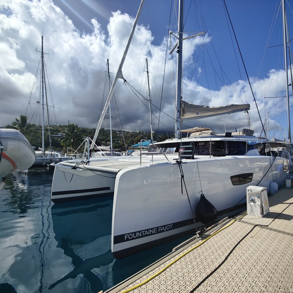 Fountaine Pajot catamaran tied to the dock. the view is from the dock looking to the white bow with a grey stripe and white fluffy clouds with blue sky after a yacht delivery