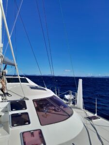 white Schionning 1600 ona delivery from New Zealand with blue sky and calm water taken from the bow looking aft with land in the bacground