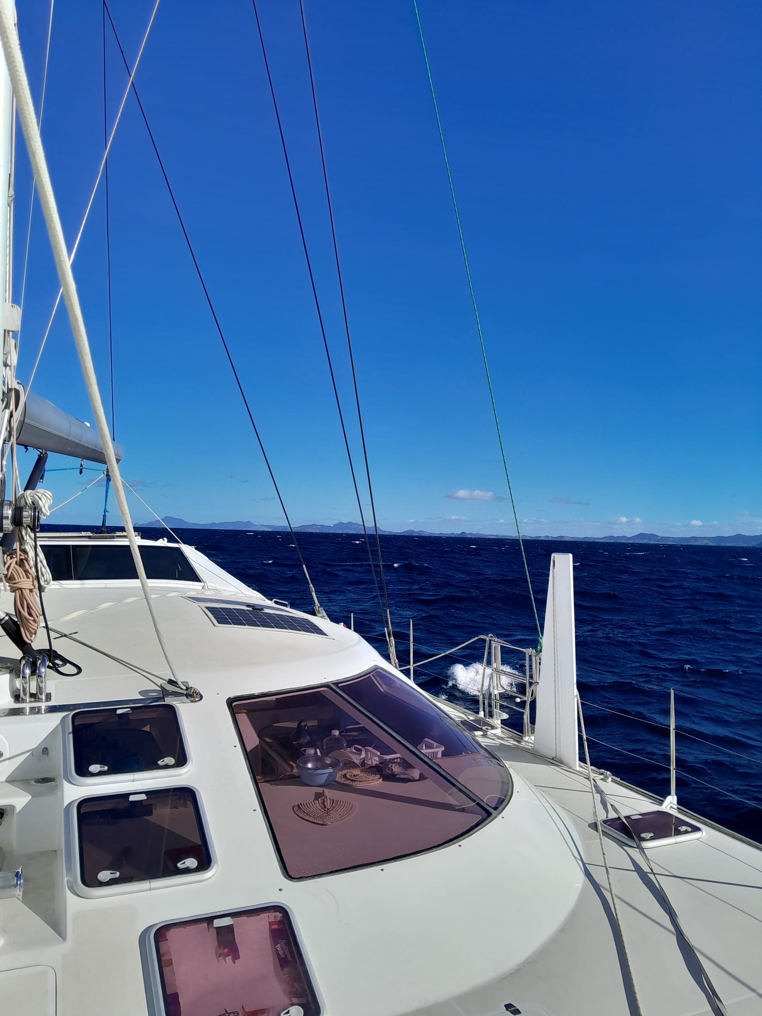 white Schionning 1600 ona delivery from New Zealand with blue sky and calm water taken from the bow looking aft with land in the bacground